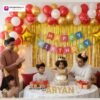 Birthday party setup with DECORATIONkart’s 66 pcs decoration kit featuring a multicolor cardstock “Happy Birthday” banner, golden fringe curtains, metallic balloons in golden, red, and white, golden star foils, and DIY accessories.