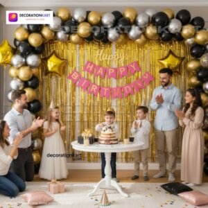 Birthday party setup with DECORATIONkart’s 66 pcs decoration kit featuring a pink cardstock “Happy Birthday” banner, golden fringe curtains, metallic balloons in golden, silver, and black, golden star foils, and DIY accessories.
