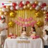 Birthday party setup with DECORATIONkart’s 66 pcs decoration kit featuring a pink cardstock “Happy Birthday” banner, golden fringe curtains, metallic balloons in golden, red, and white, golden star foils, and DIY accessories.