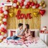 Romantic couple party setup with DECORATIONkart’s 57 pcs decoration kit featuring a red foil “LOVE” banner, golden fringe curtains, metallic balloons in red, golden, and white, heart foil balloons, and DIY accessories.