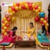 Mehndi ceremony setup with DECORATIONkart’s 59 pcs decoration kit featuring a golden foil “Mehndi” banner, golden fringe curtains, metallic balloons in golden, yellow, and red, multicolor star foils, and DIY accessories.