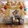 Welcome party setup with DECORATIONkart’s 60 pcs decoration kit featuring a golden foil “WELCOME” banner, golden fringe curtains, metallic balloons in pink, golden, and white, star foil balloons, and DIY accessories.