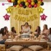 Baby shower party setup with DECORATIONkart’s 63 pcs decoration kit featuring a golden foil “Baby Shower” banner, golden fringe curtains, metallic balloons in black, yellow, and red, multicolor star foils, and DIY accessories.