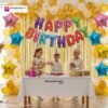 Indian children celebrating a birthday party with DECORATIONkart’s 66 pcs decoration combo set, featuring a multicolor foil “Happy Birthday” banner, golden fringe curtains, metallic balloons in gold, yellow, and white, colorful star foil balloons, and DIY accessories.