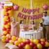 Indian children celebrating a birthday party with DECORATIONkart’s 66 pcs decoration combo set, featuring a pink foil “Happy Birthday” banner, golden fringe curtains, metallic balloons in gold, yellow, and red, pink star foil balloons, and DIY accessories.