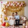 Anniversary party setup with DECORATIONkart’s 69 pcs decoration kit featuring a golden foil “Happy Anniversary” banner, golden fringe curtains, metallic balloons in golden, pink, and white, golden and red heart foils, and DIY accessories.