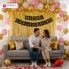 Anniversary party setup with DECORATIONkart’s 69 pcs decoration kit featuring a black cardstock “Happy Anniversary” banner, golden fringe curtains, metallic balloons in golden, pink, and white, golden and red heart foils, and DIY accessories.