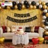 Anniversary party setup with DECORATIONkart’s 69 pcs decoration kit featuring a black cardstock “Happy Anniversary” banner, golden fringe curtains, metallic balloons in golden, silver, and black, golden and red heart foils, and DIY accessories.